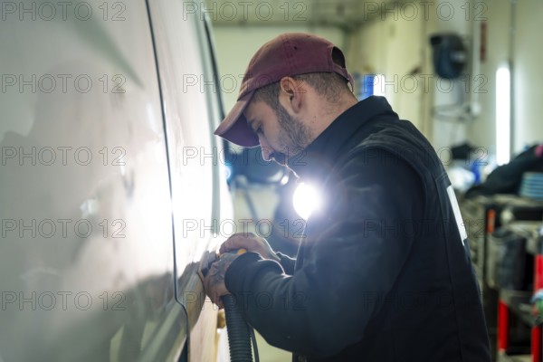 Auto body technician focused on sanding a vehicle's surface with an orbital sander, preparing the car for painting and refinishing in a professional repair shop