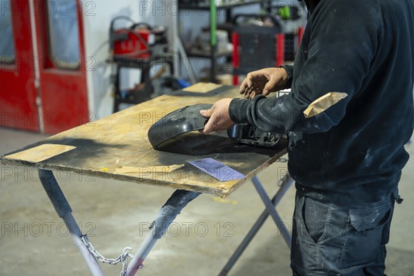 Mechanic preparing a car part by carefully sanding the surface on a workbench, ensuring a smooth finish for painting and body repair at an automotive workshop