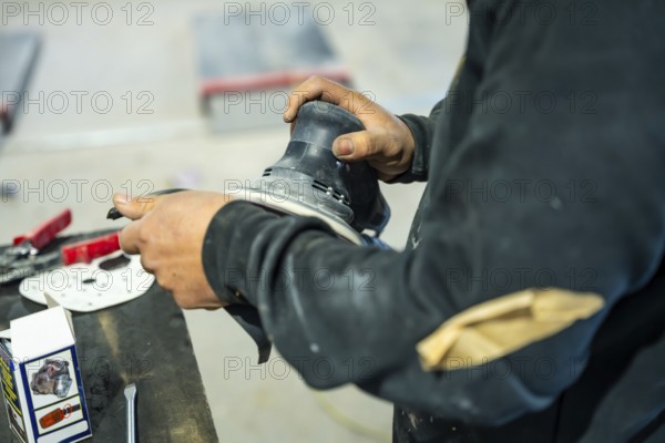Auto body technician preparing a car surface for painting using an orbital sander, demonstrating precision and hard work in a professional workshop environment