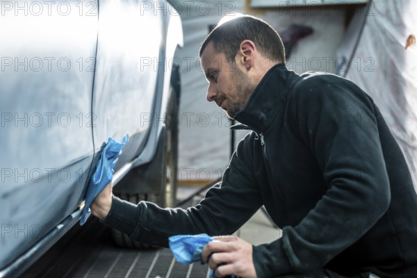 Focused mechanic carefully smooths and cleans car body surface before painting inside a modern auto repair and detailing workshop, ensuring precision and high quality vehicle finish