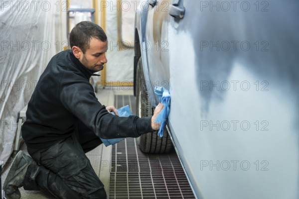 Auto body technician in a workshop cleaning and preparing a car door for painting with a microfibre cloth, ensuring a smooth surface for repair and refinishing