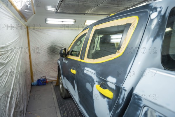Vehicle in a body shop prepped for painting, masked with tape over windows and trim, primed and sanded, ready for refinishing in a clean spray booth environment