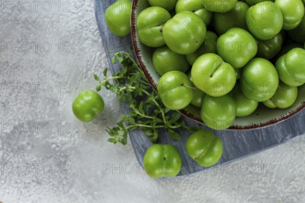 Tkemali, green cherry plum, in a bowl, on a gray table, top view, natural light, no people