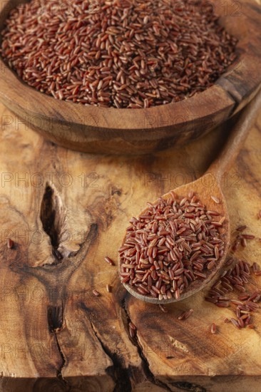 Natural, red rice, in a wooden bowl and spoon on a wooden surface in rustic style, top view