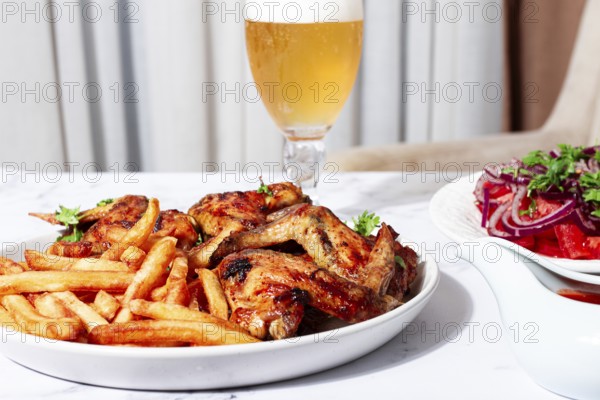 Delicious barbecue chicken wings, with French fries, salad and a refreshing drink, at a cozy table, there are no people