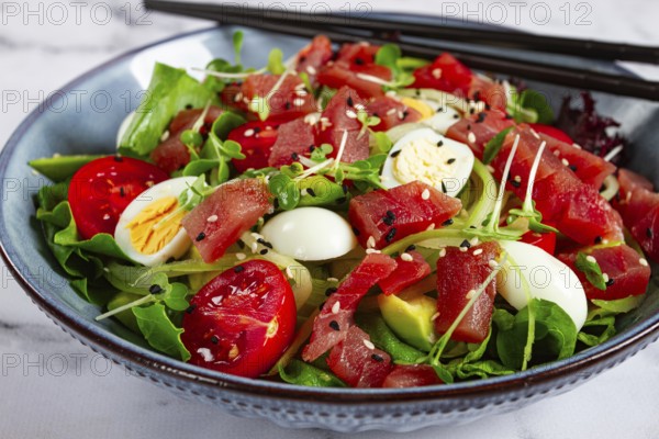 Salad with fresh tuna, cherry tomatoes and quail eggs and avacado, served with chopsticks