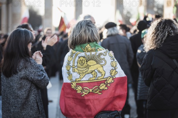 A woman wrapped in a flag of Iran during the Pahlavi period during the demonstration by exiled Iranians under the slogan Freedom for Iran led by Prince Reza Pahlavi in Berlin, Brandenburg Gate on 01.03.2026. The reason for the meeting is the joint attack by Iran by Israel and the USA and the resulting death of the previous leader Ali Khamenei