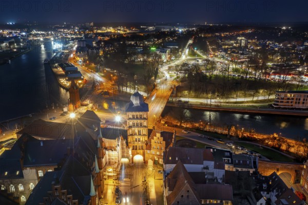 Aerial view over the Gothic Burgtor, medieval northern town gate of Hanseatic city Lübeck, illuminated at night, Schleswig-Holstein, Germany