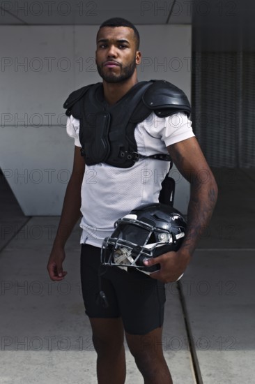 A focused football player stands with his helmet, dressed in shoulder pads and uniform, representing strength and determination in the sport. Ideal for sports-themed projects