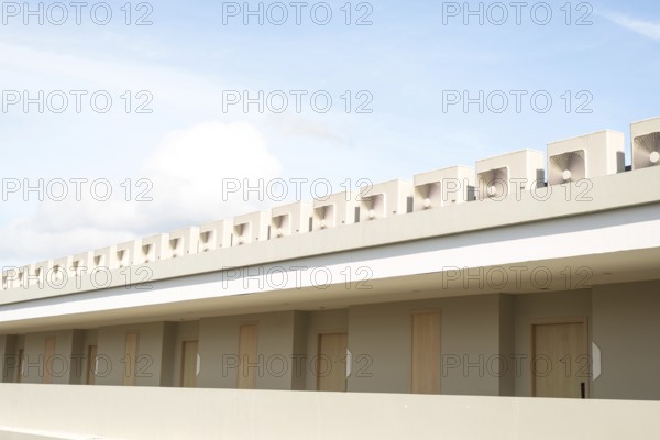 A minimalist building showcases its clean lines and neutral tones under a bright blue sky with light clouds in Thailand. The design emphasizes simplicity and functionality