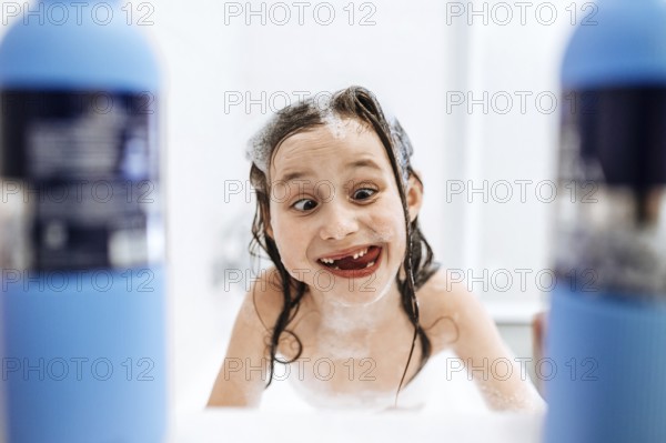 A joyful child enjoys bath time, playfully covered in foam and surrounded by bubbles, exuding happiness and innocence in a bright bathroom setting