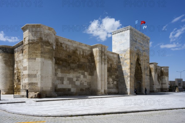 Impressive stone wall with high gate under blue sky with waving flags, Sultanhani caravanserai, on the former Silk Road, museum, Sultanhani Kervansaray, Sultanhani, Aksaray province, Turkey
