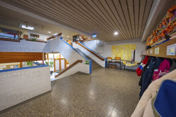 A bright corridor with cloakroom, colorful wall art and a modern wooden staircase, Schlehengäu Grund Schule Gechingen, Calw district, Germany