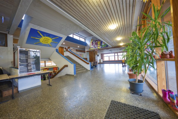 A corridor with stairs, decorated with plants and works of art, wooden ceiling, well-lit, Schlehengäu Grund Schule Gechingen, Calw district, Germany