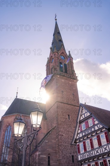Church tower in sunlight next to a traditional half-timbered house under a clear sky, Calw, Calw district, Germany