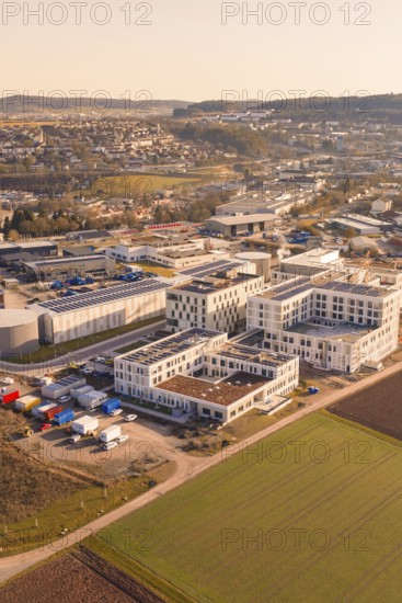 Aerial view of an industrial plant with modern buildings and surrounding fields in warm sunlight, new hospital at Calw Health Campus, Calw district, Germany