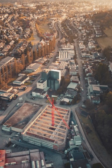 City view with construction crane in the midst of buildings and roads in the setting sun, Neubau Rewe, Aidlingen, Böblingen district, Germany