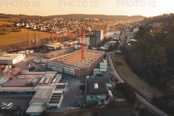 Urban scene with construction crane surrounded by residential areas and rolling hills at dusk, Neubau Rewe, Aidlingen, Böblingen district, Germany