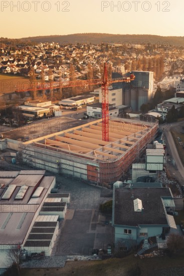 Industrial area with crane and new buildings in sunset light, on the edge of a city in a hilly landscape, Rewe new building, Aidlingen, Böblingen district, Germany