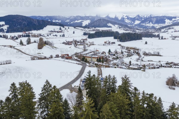 Wide view of snowy village in mountainous winter landscape with clouds in the sky, specialist clinic for psychosomatics and psychotherapy, Hochgrat Clinic, Stiefenhofen, Bavaria, Germany