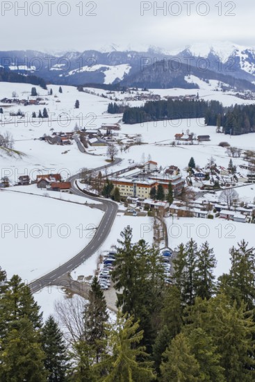 Snowy village in the mountains with a winding road surrounded by trees and cloudy sky, specialist clinic for psychosomatics and psychotherapy, Hochgrat Clinic, Stiefenhofen, Bavaria, Germany