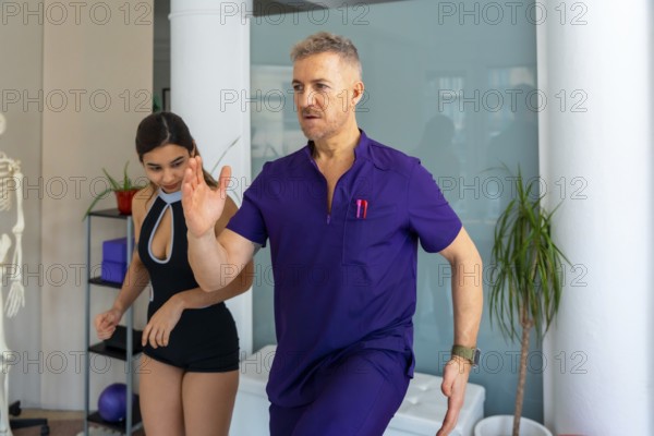 Professional physiotherapist in purple scrubs guiding a young female patient through a rehabilitation exercise for physical recovery and improved mobility in a medical clinic setting