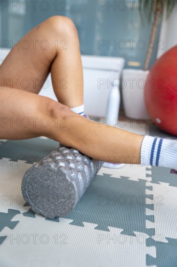 Person's legs performing self myofascial release actively with a foam roller, focusing on muscle recovery, pain relief, and rehabilitation on a floor mat