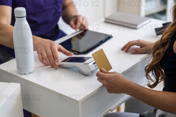 Patient making a contactless payment with a gold credit card on a pos terminal at a medical clinic reception, after receiving physiotherapy or osteopathy treatment