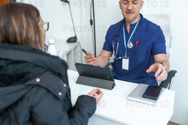 Male doctor wearing scrubs and stethoscope explaining healthcare data to a female patient during a digital medical consultation in a modern clinical office setting