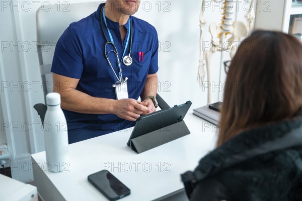 Healthcare professional reviews digital records on a tablet while consulting with a patient in a modern clinic office, discussing diagnosis, treatment options and care plans