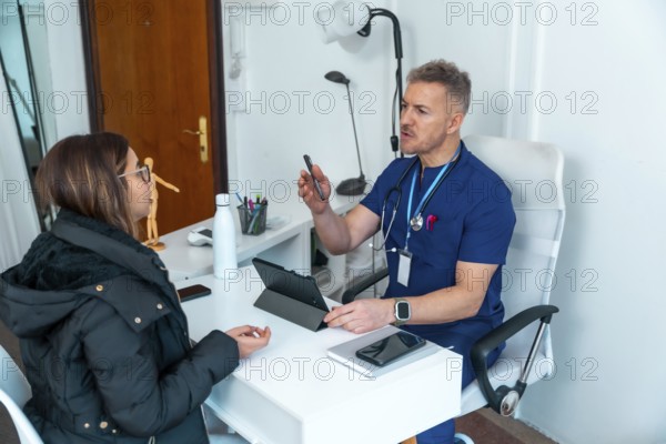Doctor in scrubs having a conversation with a female patient during a medical consultation at a clinic office, providing information and discussing health issues