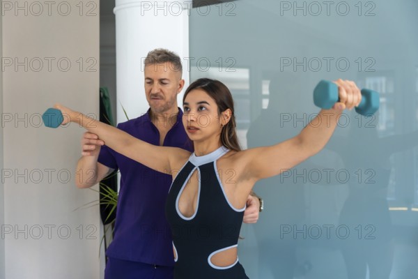 Young woman training with light dumbbells for sports recovery, guided by an experienced physiotherapist, focusing on muscle rehabilitation and injury prevention