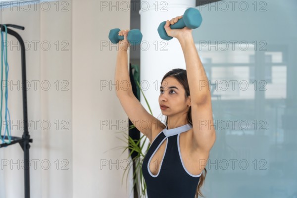 Young woman performing a strength workout with dumbbells, focusing on rehabilitation and medical recovery exercises in a home gym or physiotherapy setting