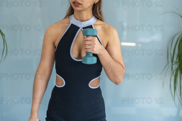 Young woman working out with a light dumbbell, focusing on strength and flexibility during a personal training session or rehabilitating through sports physiotherapy exercises