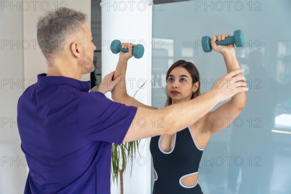 Physiotherapist assisting a young woman with a therapeutic exercise, guiding her arm while she lifts dumbbells, focusing on recovery from sports injury or physical rehabilitation