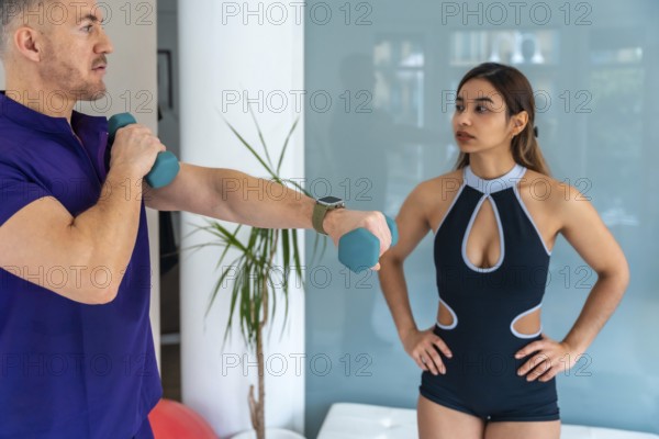 Male physiotherapist guiding a young female athlete through a rehabilitation exercise, holding light dumbbells for upper body strength, while she observes the movement