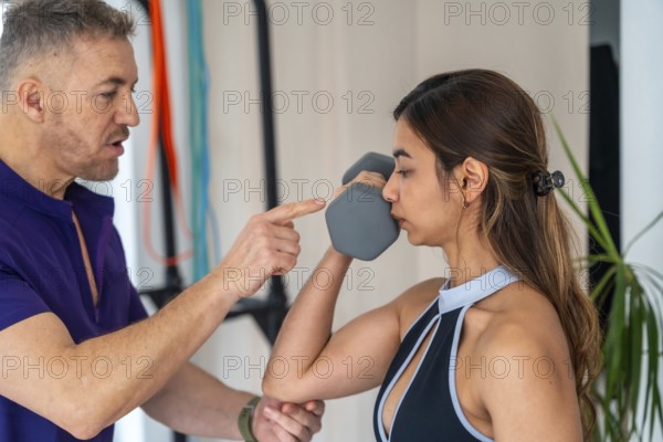 Male physiotherapist guiding a young woman performing a dumbbell exercise for rehabilitation and muscle strengthening, focusing on proper form in a professional clinic setting