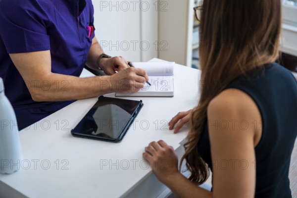 Medical professional, possibly an osteopath or physiotherapist, discussing treatment plans and rehabilitation programs with a female patient during a consultation in a clinic setting