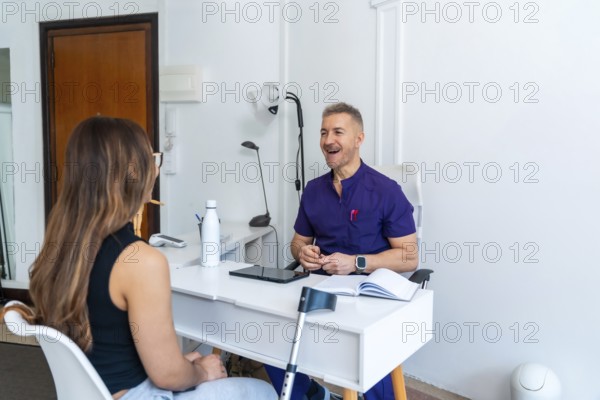 Experienced male physiotherapist in purple uniform consulting young female patient in modern clinic about sports osteopathy, rehabilitation and treatment options after injury