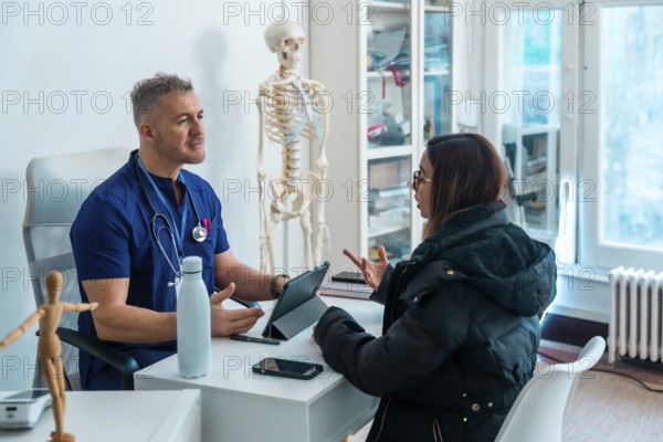 Doctor in blue scrubs and stethoscope consulting a female patient regarding her health concerns, discussing treatment options in a modern medical office setting with a skeleton model