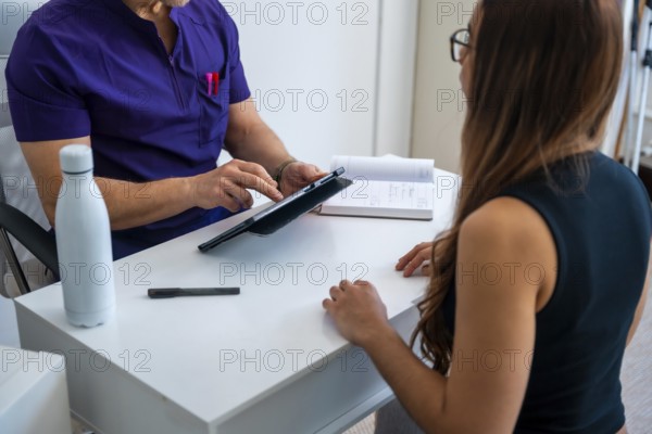 Professional osteopath or physiotherapist doctor in medical scrubs consulting a female patient, reviewing health data on a tablet for a sports injury or rehabilitation session