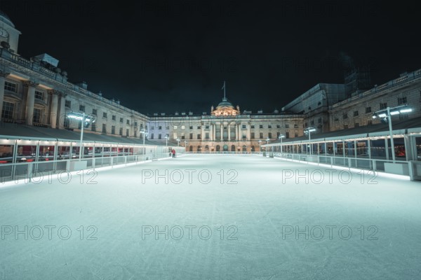 Empty ice rink at night surrounded by a symmetrical historic building, London, United Kingdom