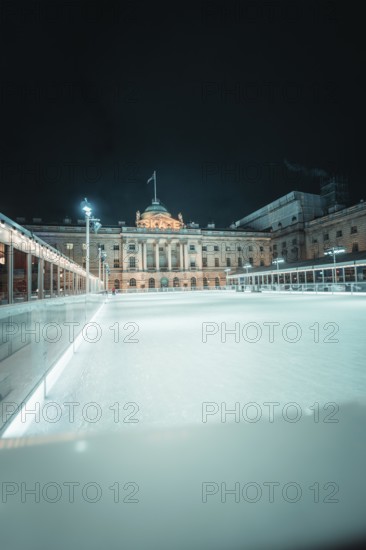Large empty ice rink in front of an illuminated building at night, London, United Kingdom