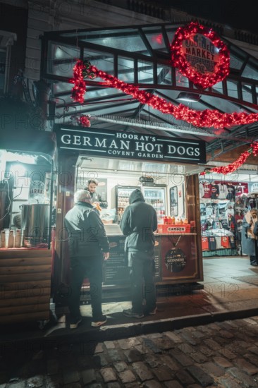 Market stall at night, decorated with Christmas lights, with people in front of it, London, Great Britain
