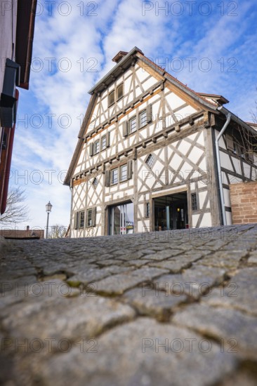 Timbered house with steep roof line against blue sky and cobblestone road, Ötisheim, Enzkreis, Germany