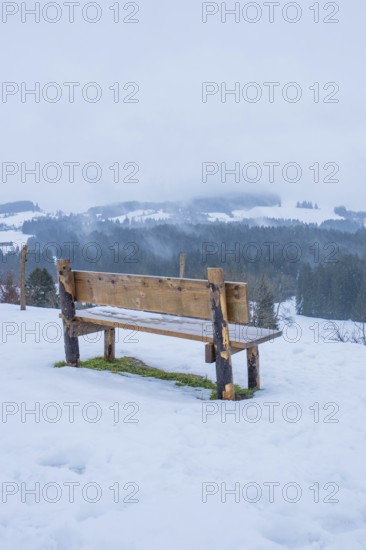 Wooden bench on snowy ground with a view of a quiet winter landscape, Sinnraum, Oberreute, Allgäu, Bavaria, Germany