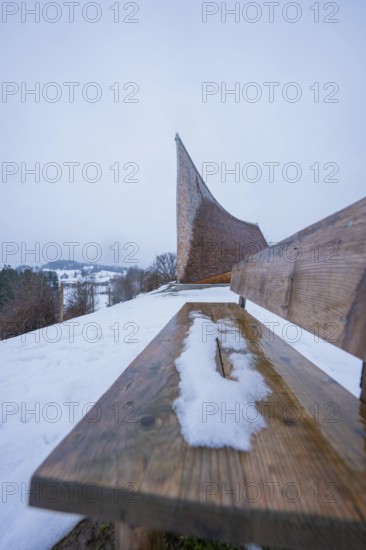 Wooden bench in snow with modern building in background and winter atmosphere, Sinnraum, Oberreute, Allgäu, Bavaria, Germany