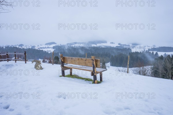 Wooden bench on snow-covered ground with view of winter landscape, Sinnraum, Oberreute, Allgäu, Bavaria, Germany