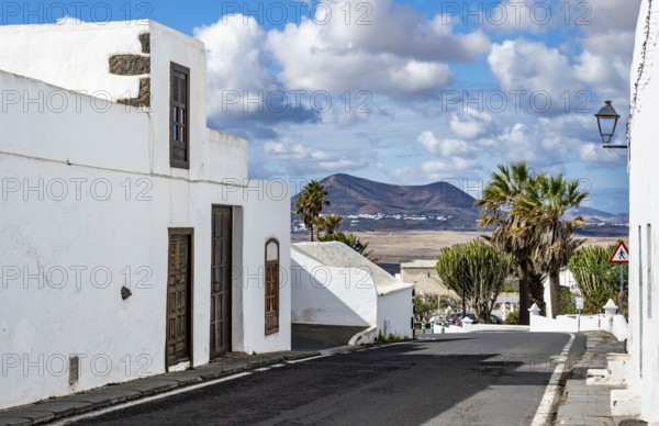 Typical white houses with colored doors and windows in an alley with volcanic craters behind, Teguise, Lanzarote, Canary Islands, Spain