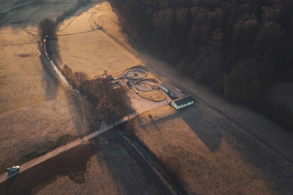 A path leads to a treatment plant with round structures, surrounded by fields and forest at sunset, Gechingen, Calw district, Germany